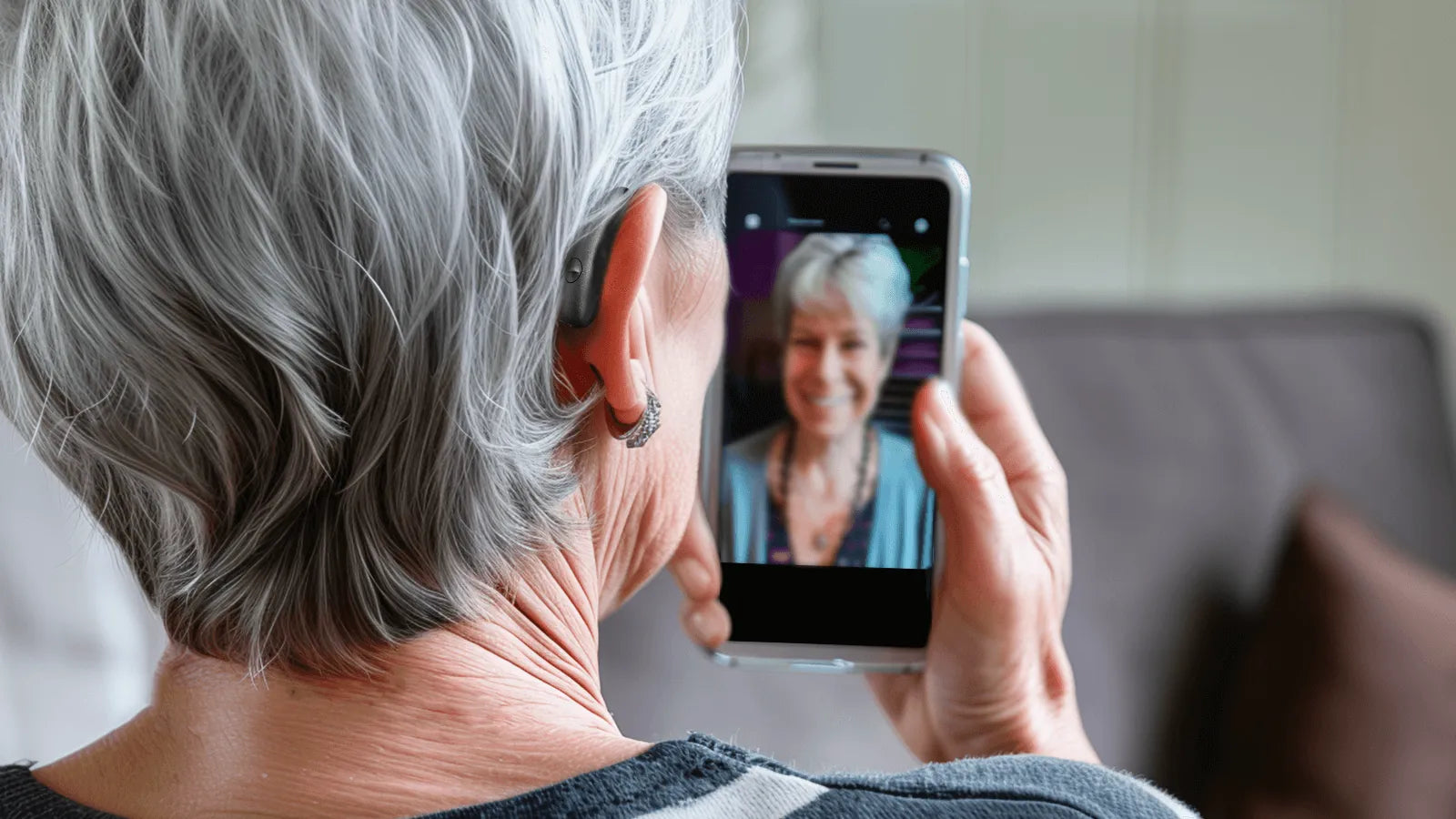 An elderly woman wearing a Beacon hearing aid and using Bluetooth functionality on her smartphone to make a phone call