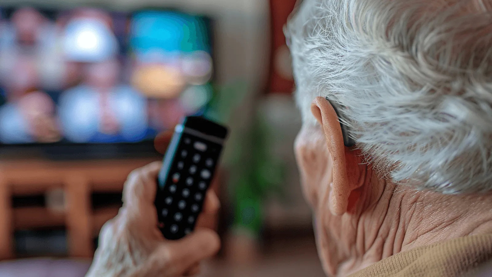 An elderly person wearing a Beacon hearing aid while watching television