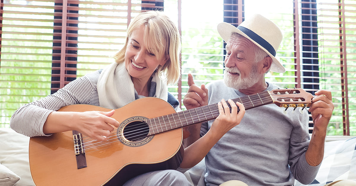 Senior couple playing guitar together in a bright room.