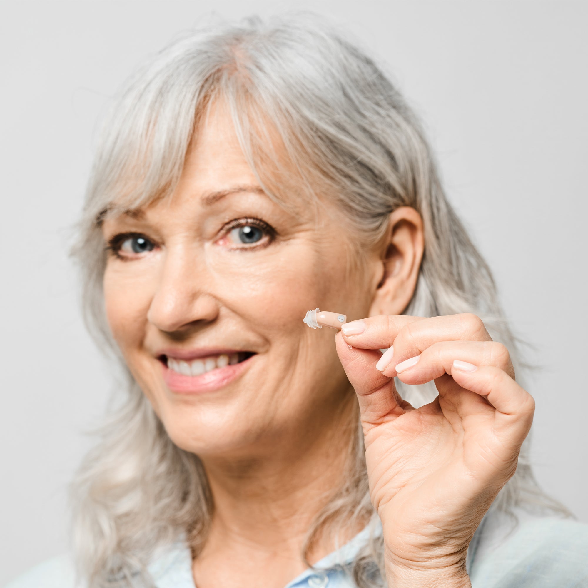 Woman holding a clear Core One Pro hearing aid against a light background