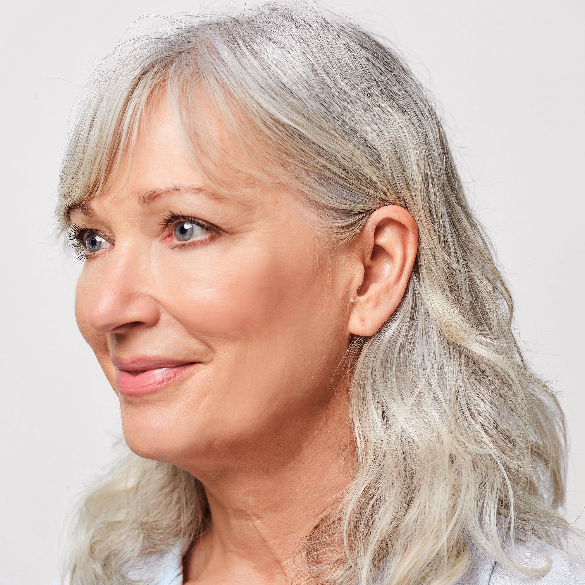 A woman with gray hair smiling, wearing Core One Pro hearing aids in her ear.