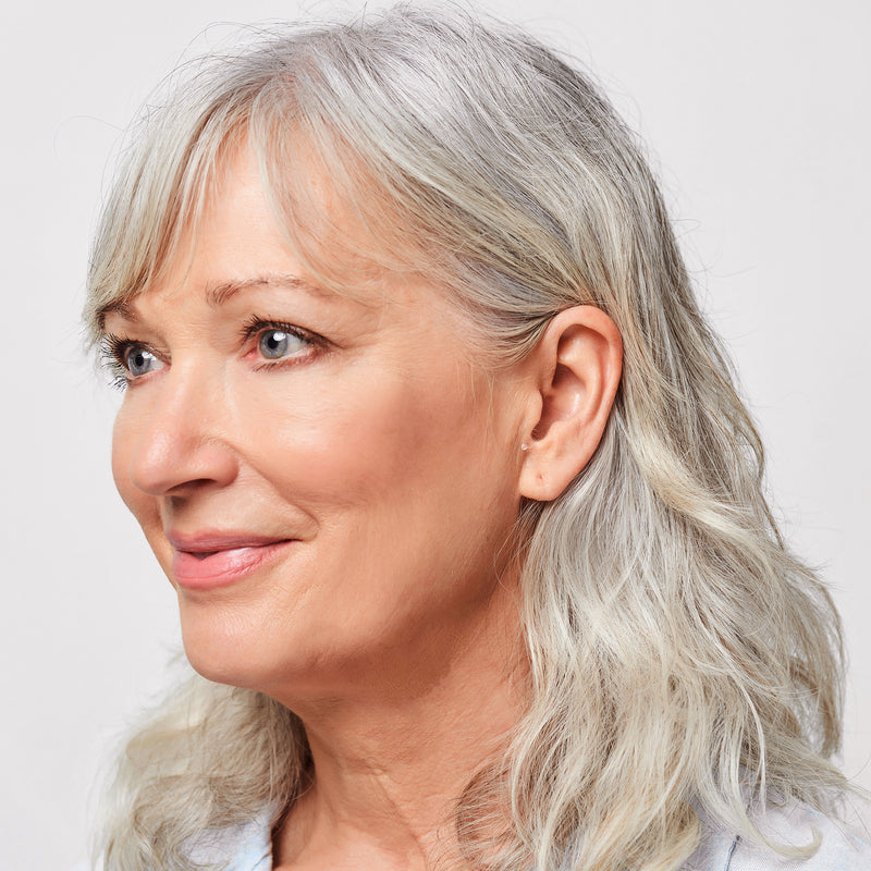 A woman with gray hair smiling, wearing Core One Pro hearing aids in her ear.