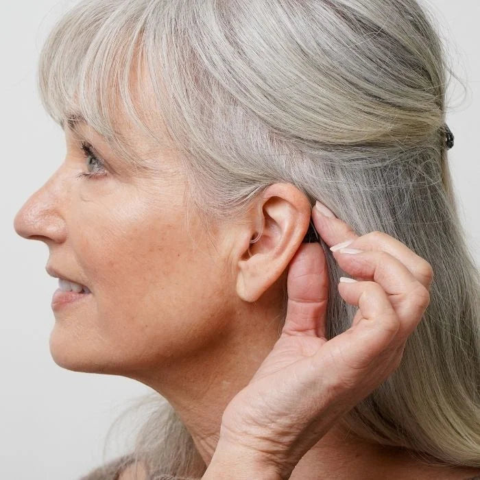 Ceretone Nexus over the counter hearing aid behind the ear adjusting the  volume and settings with accessible buttons on the hearing aids. 
